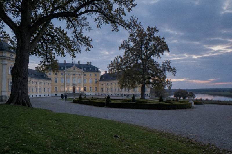 The pale yellow Baroque Rogalin Palace behind a formal courtyard with ancient oaks